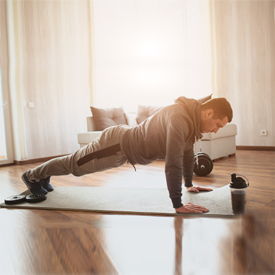 In his living room, a young fit man is doing push ups next to his sofa