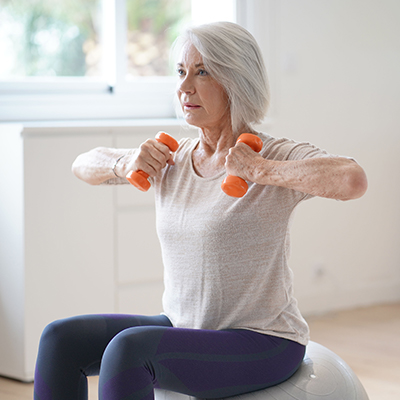 A white-haired elderly woman exercises with a mini dumbell