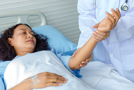A sick woman lies in a hospital bed, her pulse being checked by a doctor