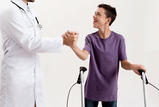 A doctor holding the hands of a physically challenged boy who is standing with his walking stick