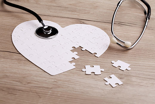 Arrangement of puzzle pieces in a heart shape on a wooden background with a stethoscope on top