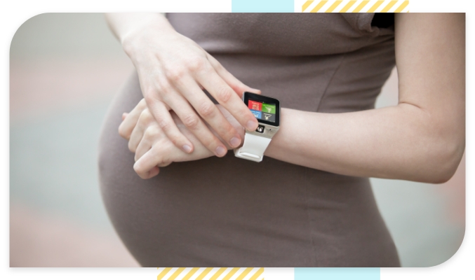 Closeup of a pregnant woman holding her smart watch in her hands while wearing light brown clothing
