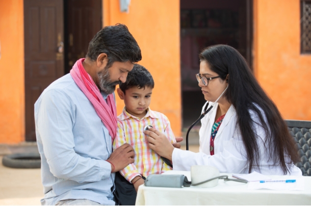 A female doctor examining a boy with his father beside.